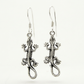 Pair of textured sterling silver lizard earrings with curled tails and French hooks on white.